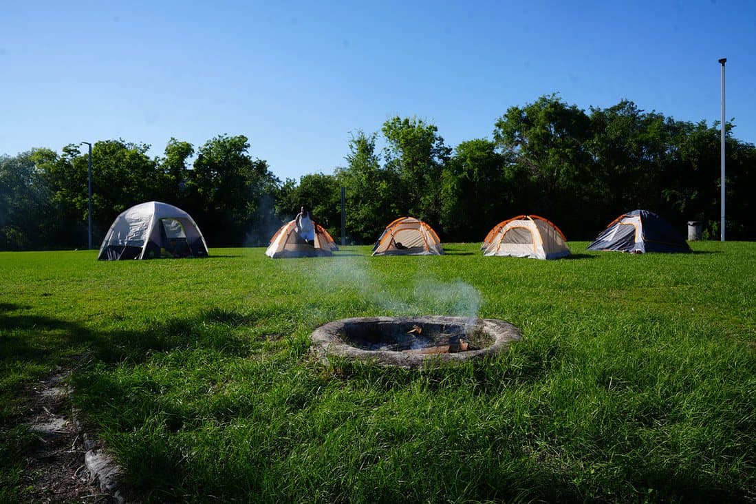 Tents on a green field around a campfire ring